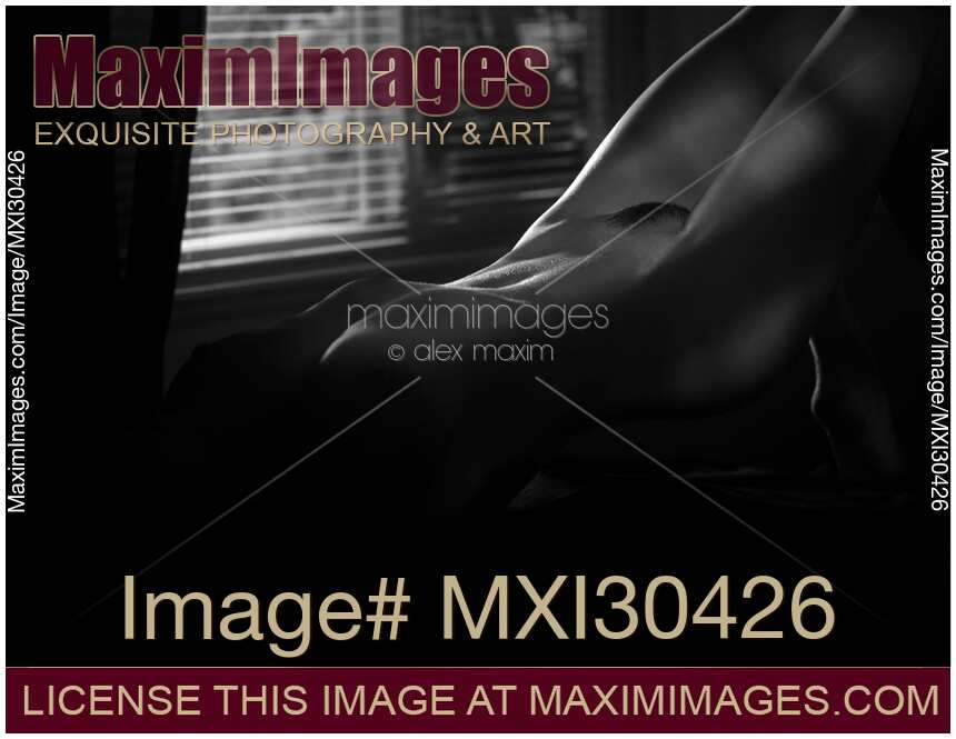 Art nude black and white photo of a sexy beautiful woman body in a dark room lit by a dim light