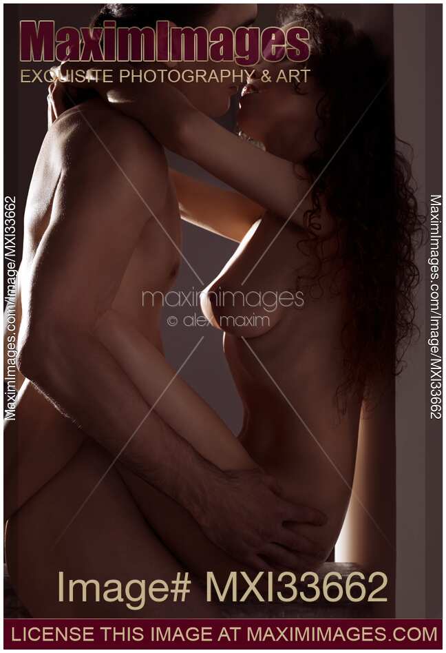 Art nude portrait of a beautiful sensual couple making love kissing with dim light outlining their naked bodies