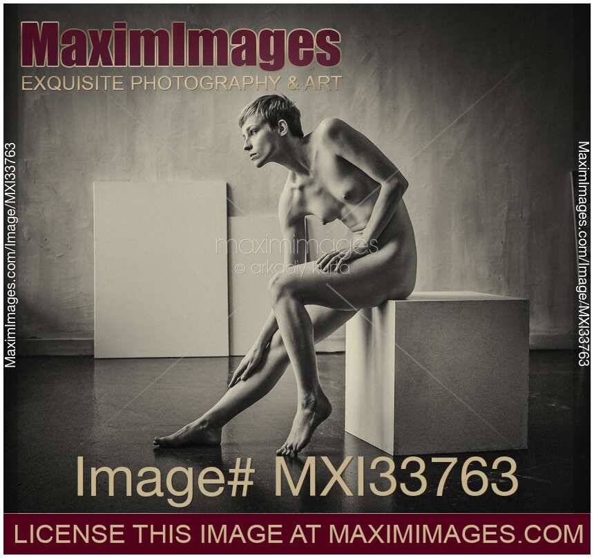 Art nude portrait of woman sitting naked on a posing box in artist studio. Black and white sepia.