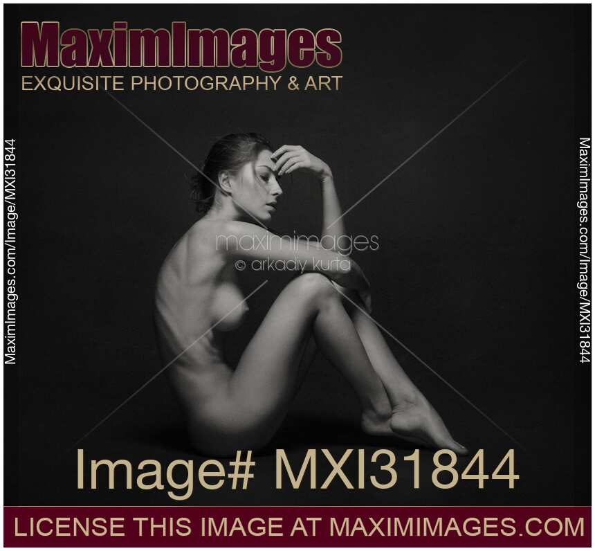 Art nude side view of a woman sitting naked in studio with black background