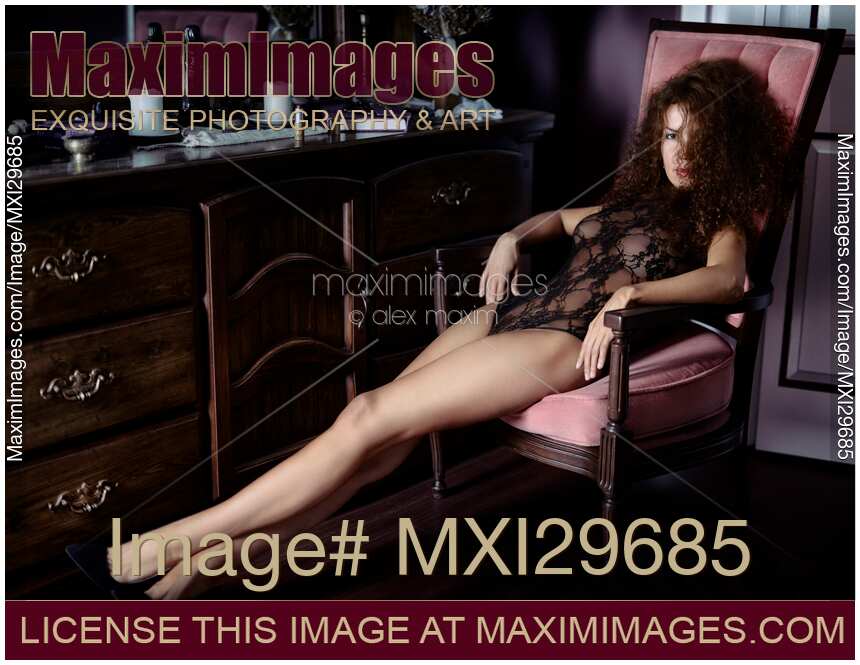 Artistic boudoir portrait of sexy woman sitting in chair by a dresser with an expressive look