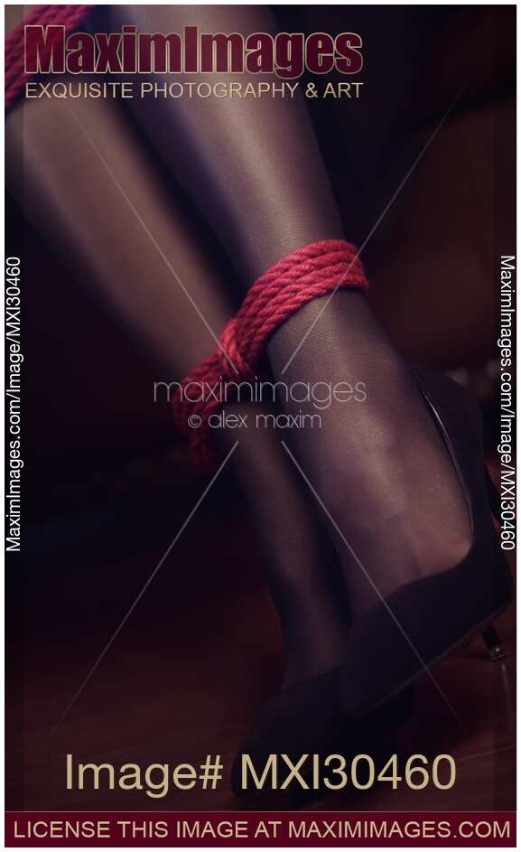 Artistic closeup of sexy woman legs with a red bondage rope around ankles