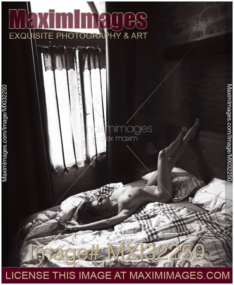 Artistic erotic black and white portrait of a nude sexy woman lying relaxed on a bed a dim bedroom