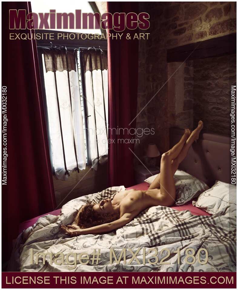 Artistic erotic portrait of a nude sexy woman lying relaxed on a bed a dim bedroom