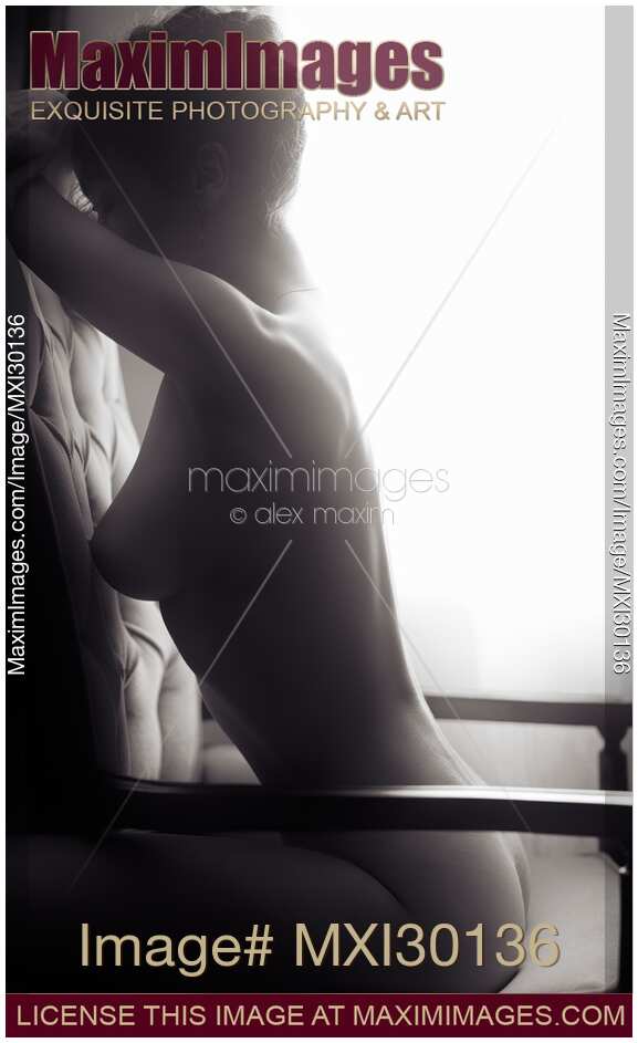 Artistic nude black and white portrait of woman sitting naked in armchair with sunlight shining on her bare back