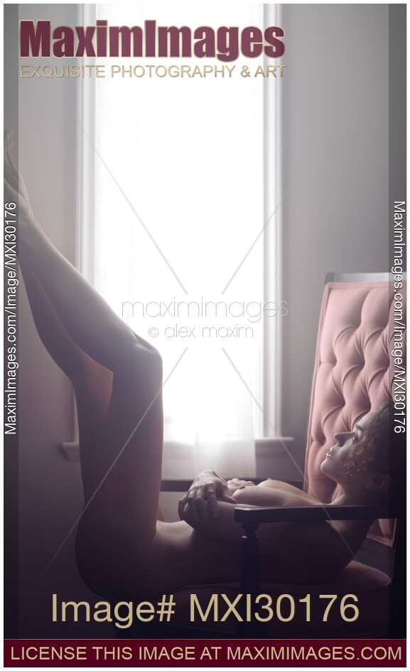 Artistic nude portrait of beautiful woman lying naked in armchair with her legs raised