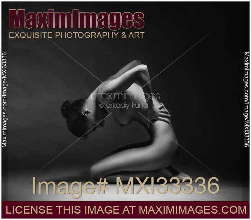 Artistic nude side view of a woman sitting naked curled up in studio with black background Black and white
