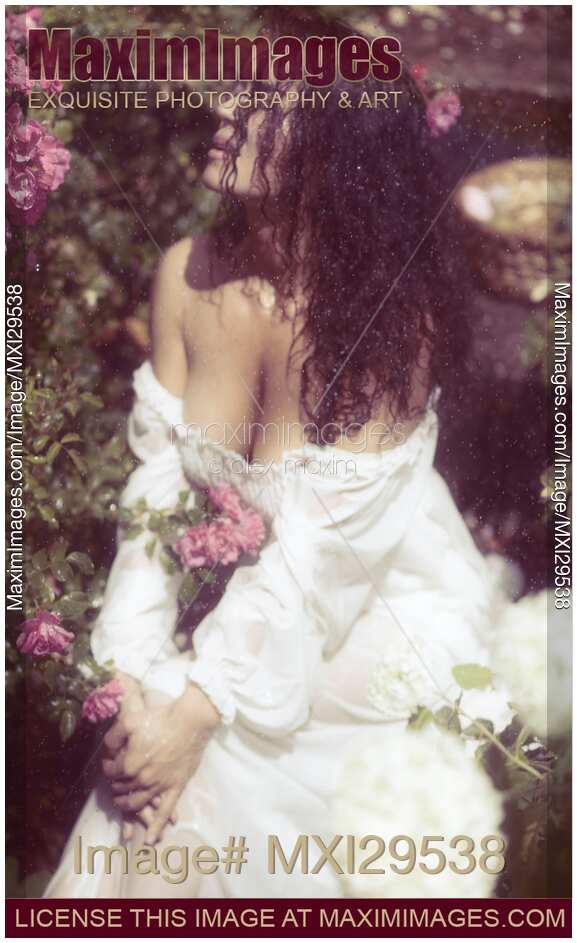 Artistic portrait of a beautiful woman in wet clothes sitting in rose garden on a rainy day