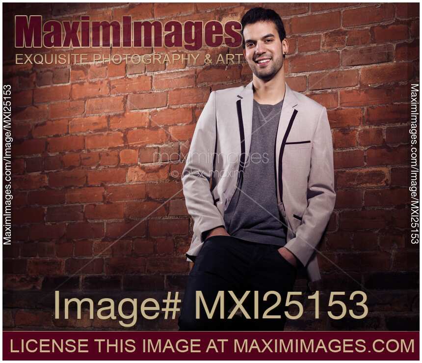 Artistic portrait of a young smiling man standing at brick wall