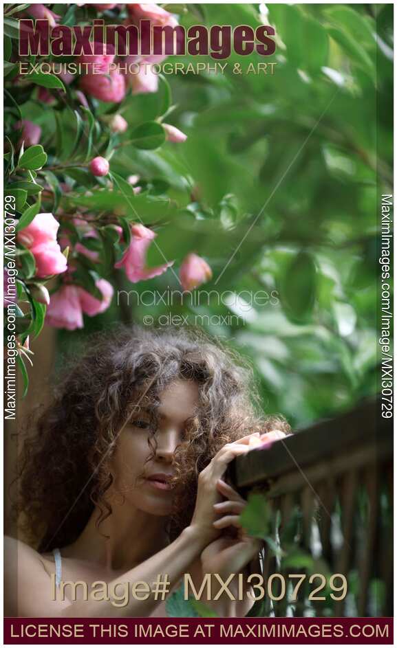 Artistic tranquil portrait of a beautiful woman standing in a garden under camellia pink flowers with a serene dreamy expression