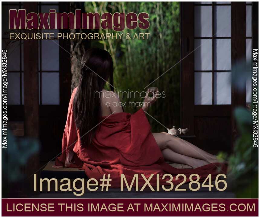 Asian woman in red kimono drinking tea half dressed by open shoji doors in a Japanese house Sensual portrait
