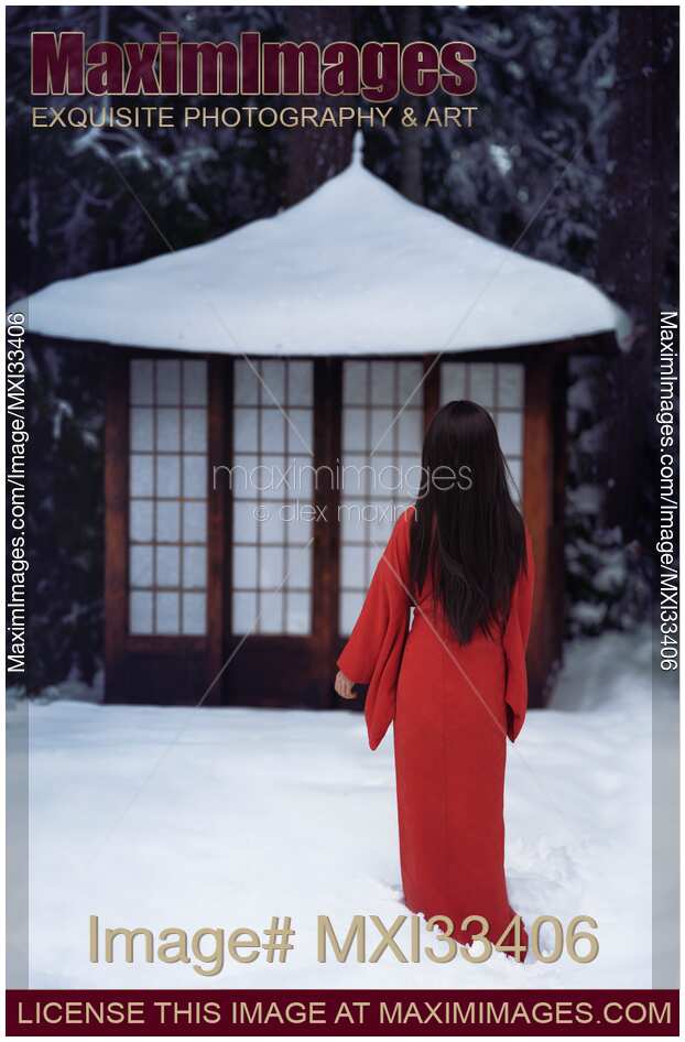 Asian woman in red kimono standing in white snow looking at a little traditional Japanese house or temple
