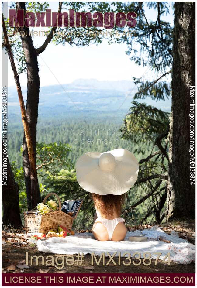 Back of a woman in big sun hat and underwear relaxing on a picnic in sunny summer nature scenery view