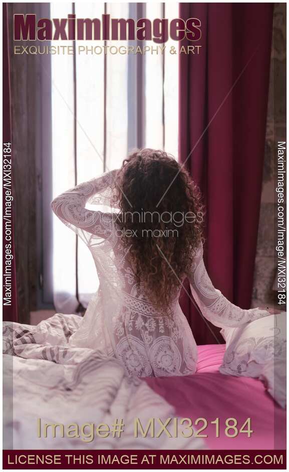 Back of a woman in white nightgown sitting on the side of the bed in the morning just awaken