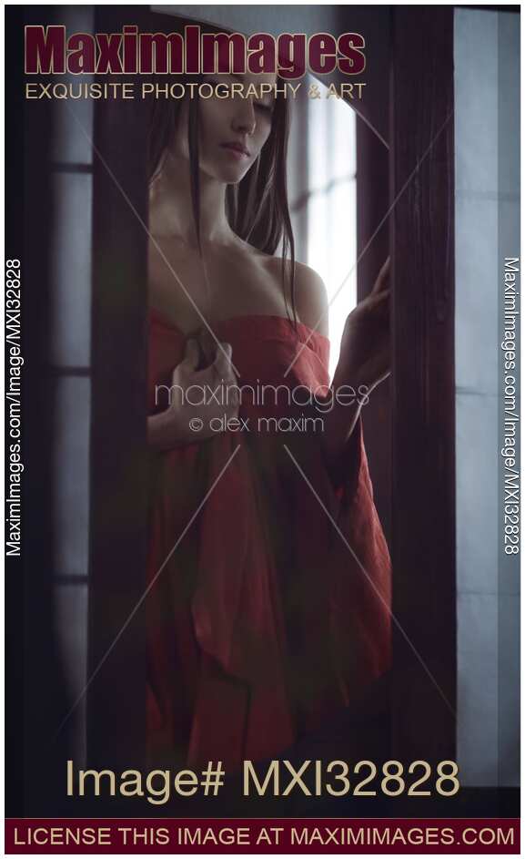 Beautiful Asian woman in undone red kimono standing by an open shoji window of a Japanese historic house Dramatic sensual portrait