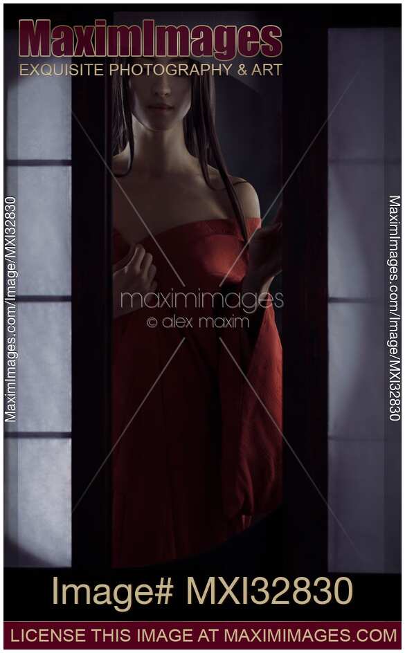 Beautiful Asian woman in undone red kimono standing by an open shoji window of a traditional Japanese house Dramatic sensual fine art portrait