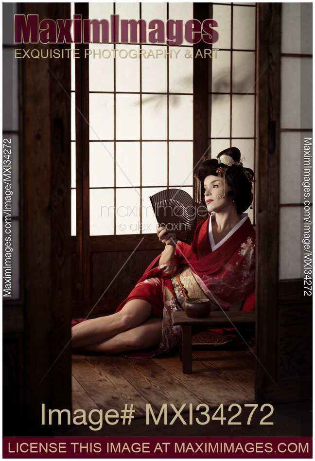 Beautiful caucasian lady, Japanese geisha sitting with hand fan in a sensual pose with her legs bared