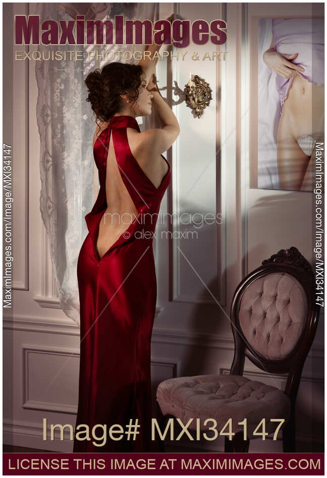 Beautiful classy elegant lady in red evening gown with open back leaning against a wall in a seductive suggestive pose