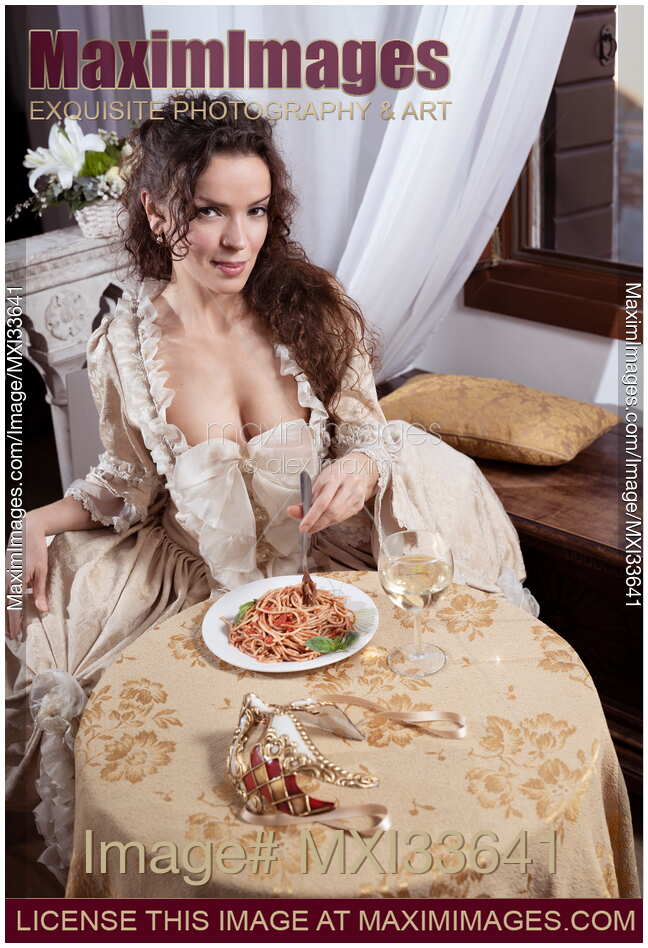 Beautiful elegant lady in vintage carnival dress eating Italian pasta sitting at restaurant table with seductive look