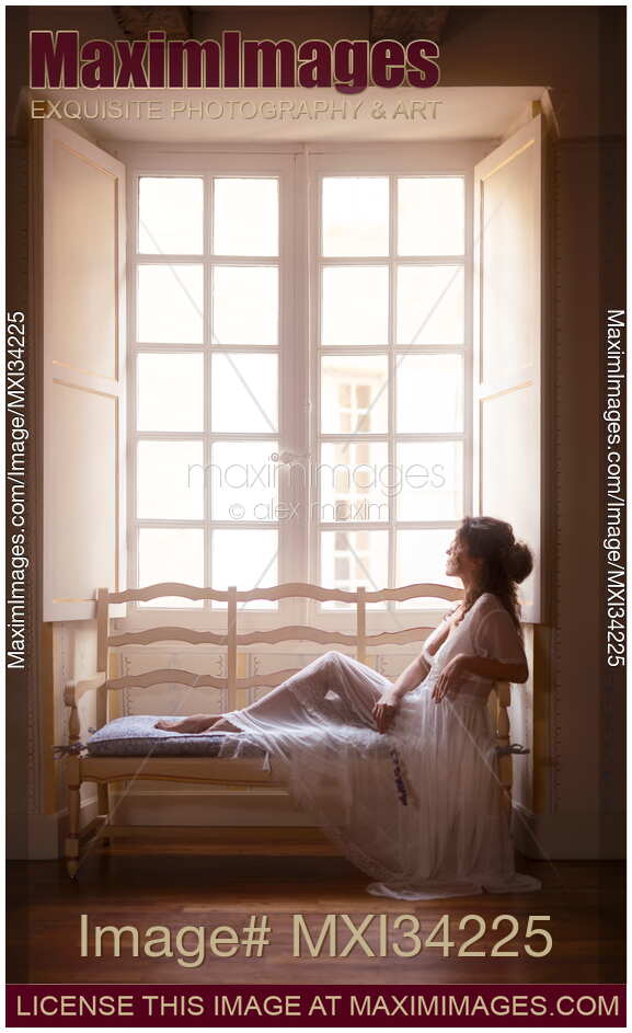 Beautiful lady in sheer white lace nightgown sitting on vintage sofa by a large French window