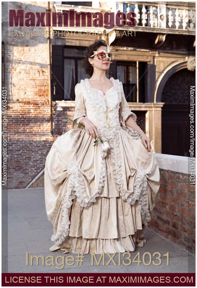 Beautiful lady in Venetian carnival costume dress and mask walking along historic street in Venice