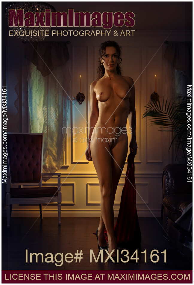 Beautiful lady with seductive enticing gaze walking naked across a dimly lit room with dress in her hand