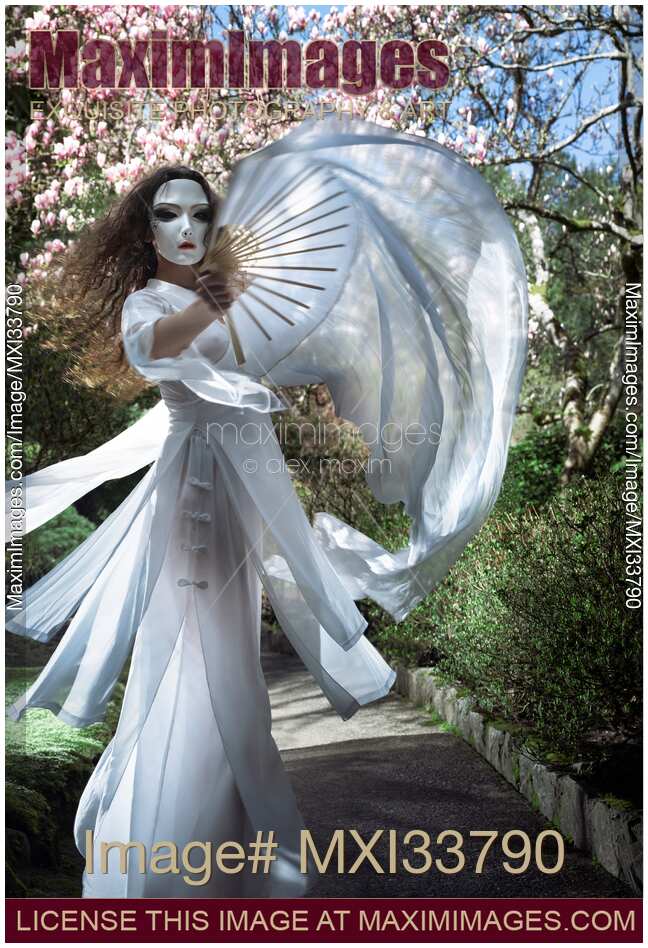 Beautiful mysterious asian woman in face mask and white gown dancing gracefully with silk fans in garden