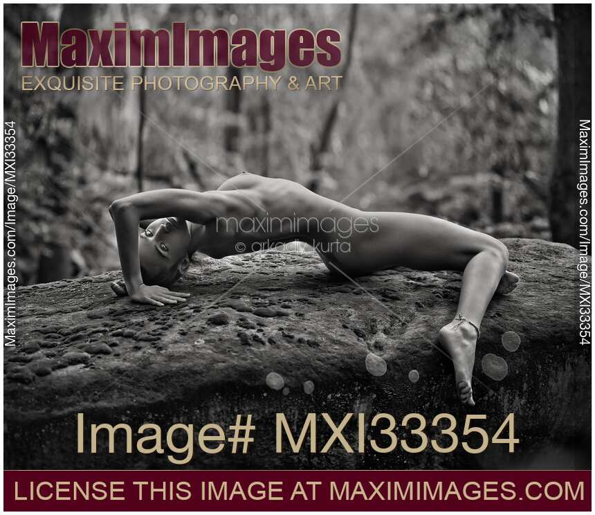 Beautiful naked woman lying in a sensual pose on rocks in the nature Black and white fine art nude