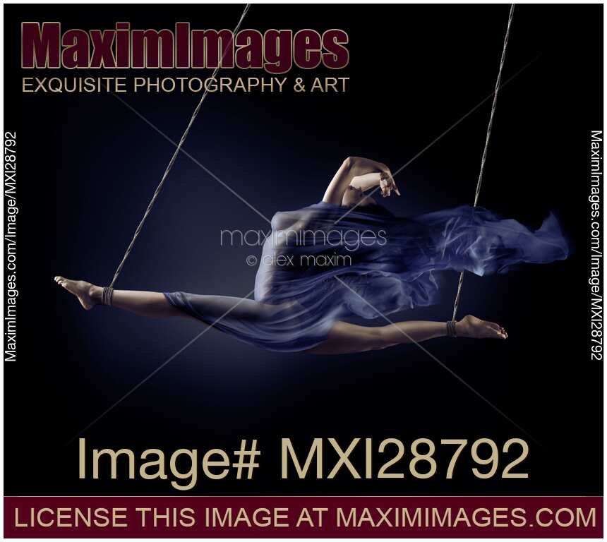 Beautiful naked woman suspended in a split with bondage ropes with flowing cloth wrapped around her nude body