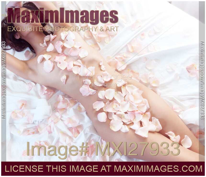 Beautiful nude asian woman lying in bed with pink rose petals on her body