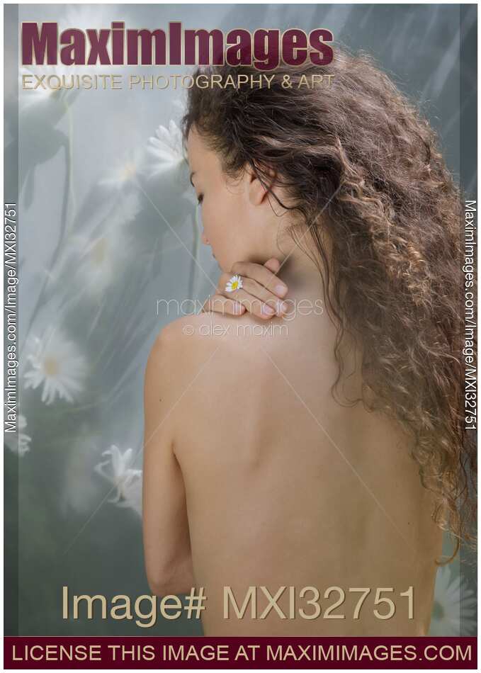 Beautiful nude woman bare back with long brown hair and a flower in her fingers in natural sunlight
