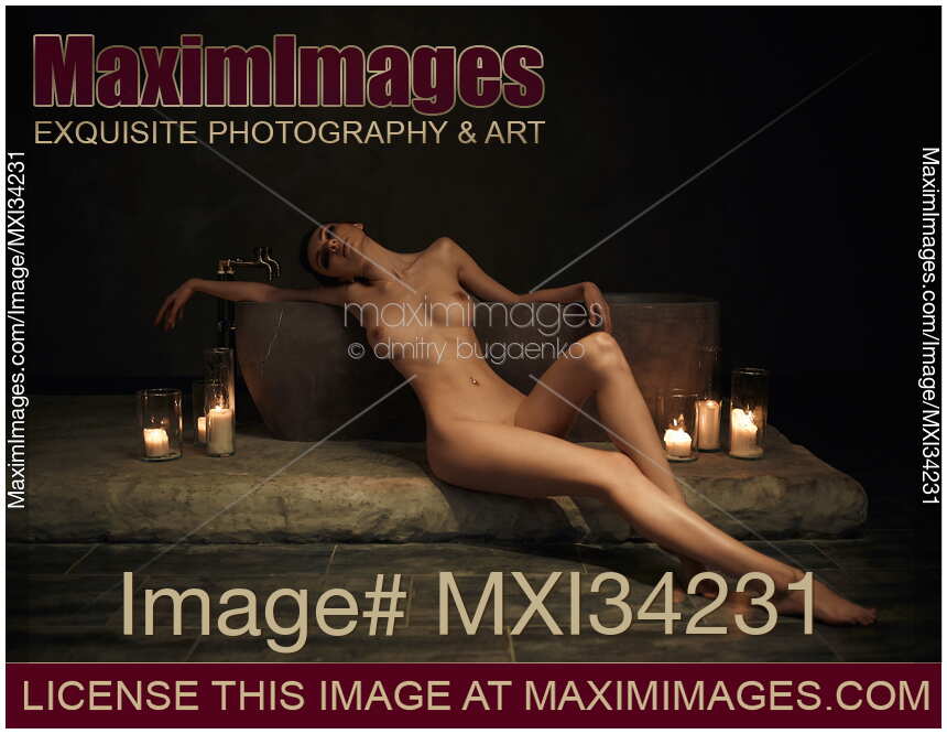 Beautiful nude woman leaning gracefully against a stone bath with candles