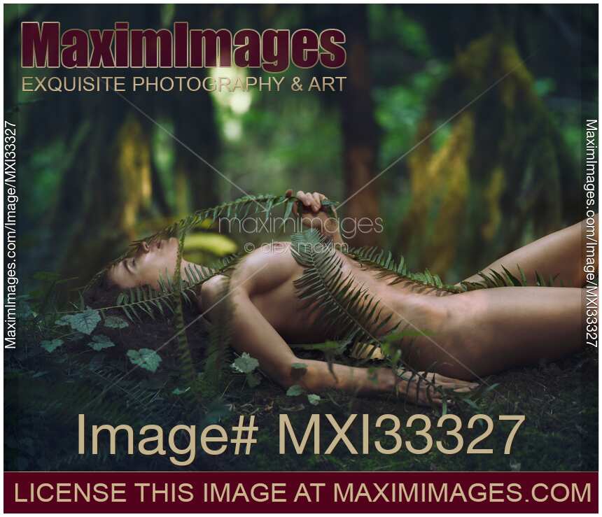 Beautiful nude woman lying on green moss in a rain forest covering her naked body with fern branches