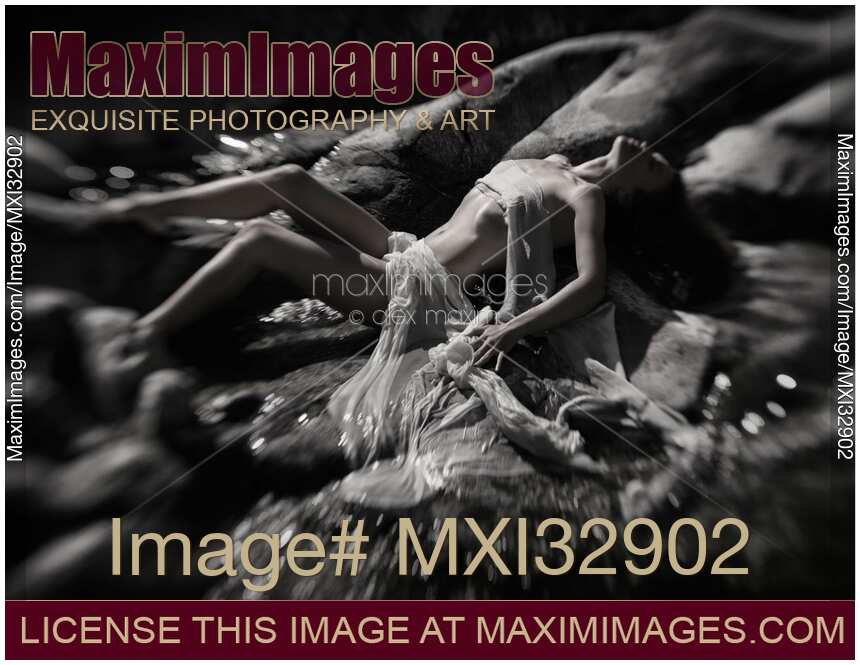 Beautiful nude woman lying on river rocks her naked barely covered body blending with rocky landscape Black and white