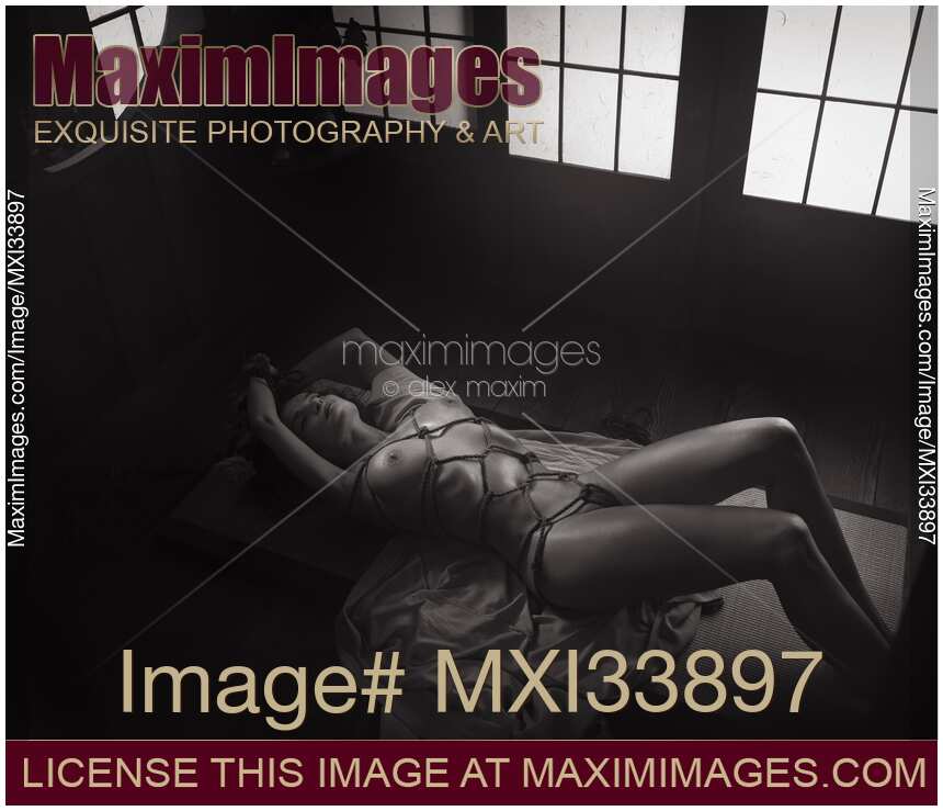 Beautiful nude woman lying on the floor tied up with red Shibari bondage ropes Sensual erotic black and white photograph