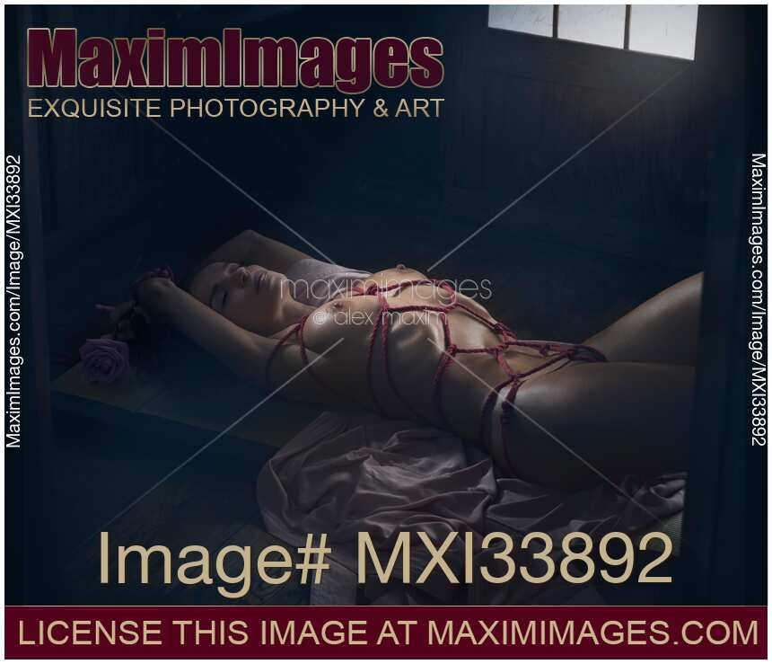 Beautiful nude woman lying on the floor tied up with Shibari bondage ropes. Sensual erotic photo.