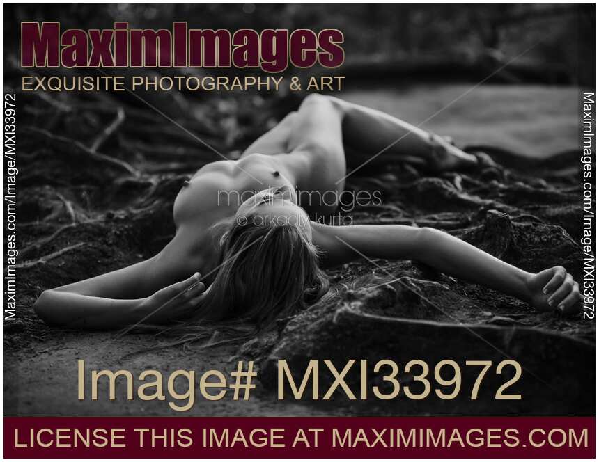 Beautiful nude woman lying on the ground with roots in a forest