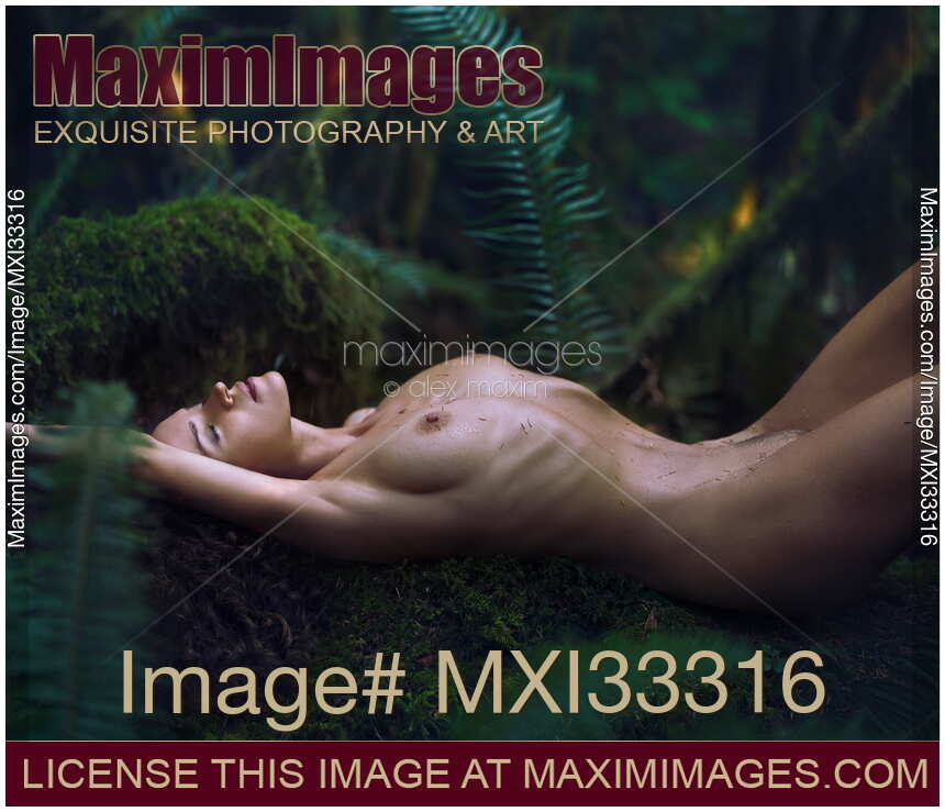 Beautiful nude woman lying relaxed on a mossy tree in green forest with rain drops on her shiny naked body
