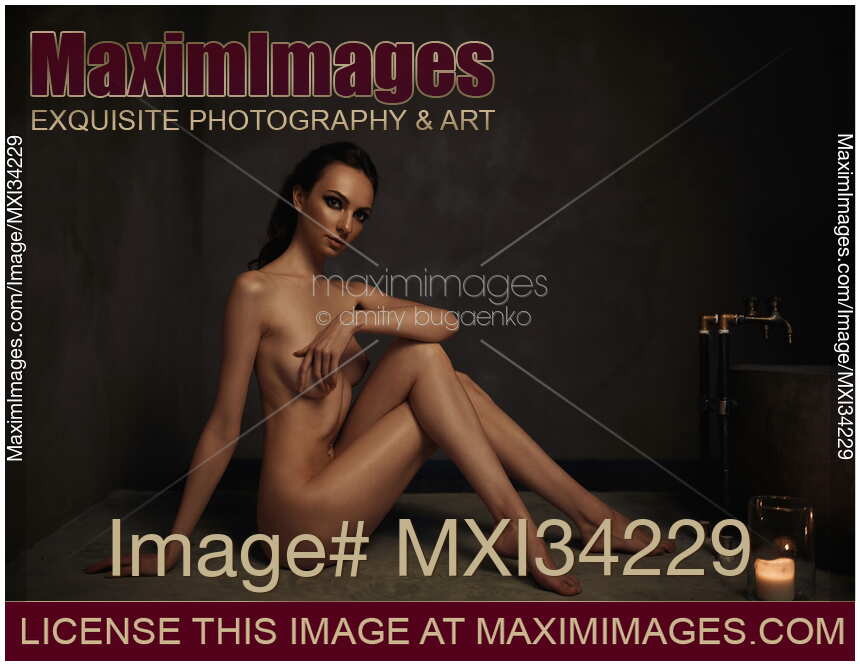 Beautiful nude woman sitting in a sensual pose in a dark bathroom