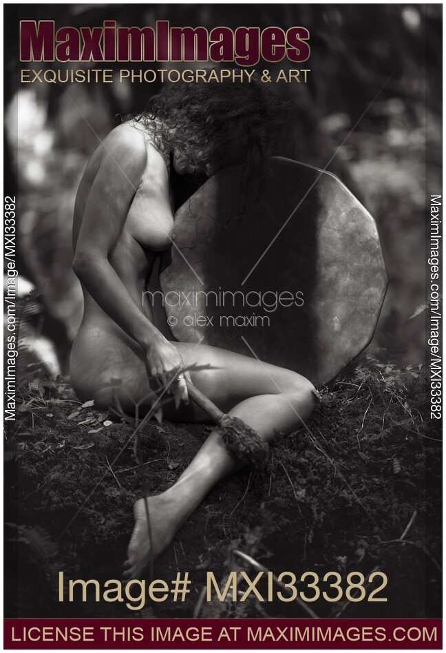 Beautiful nude woman sitting in a tranquil nature scenery leaning against a shamanic drum Black and white