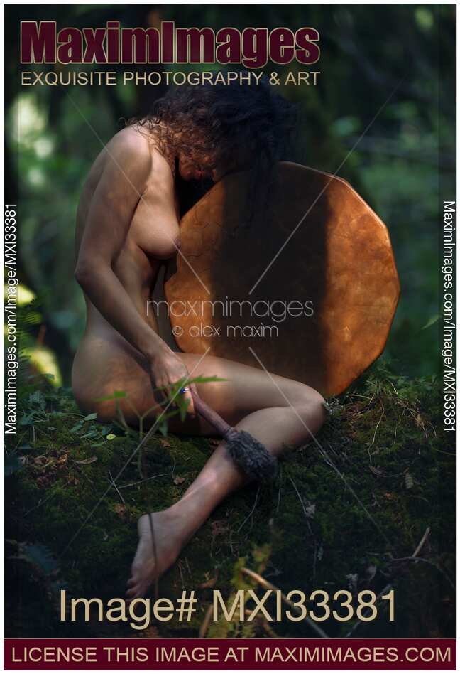 Beautiful nude woman sitting in a tranquil nature scenery leaning against a shamanic leather drum