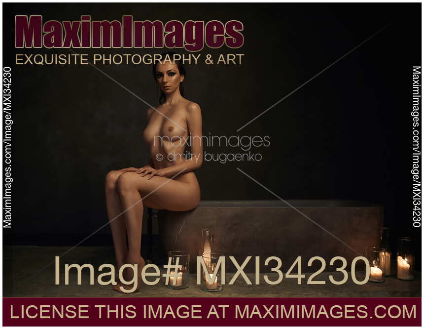 Beautiful nude woman sitting on the edge of a stone bath with candles