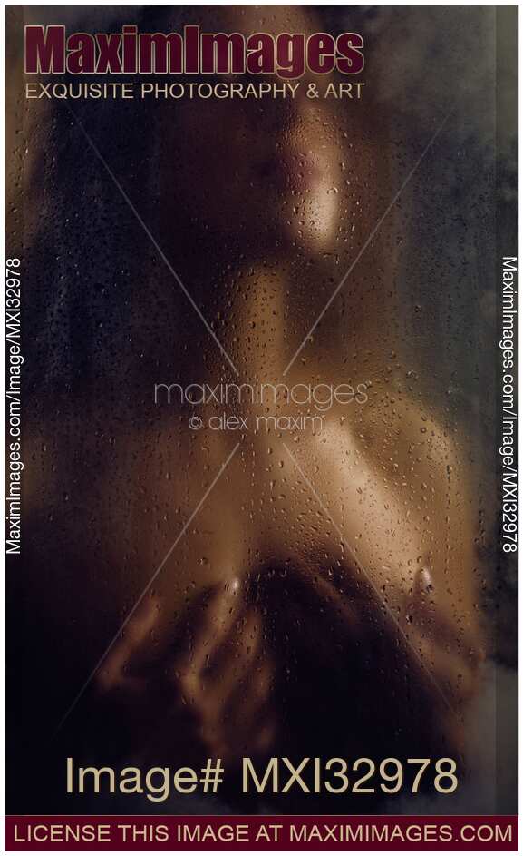 Beautiful nude woman with her hands holding her breasts behind a wet hazy glass in dark