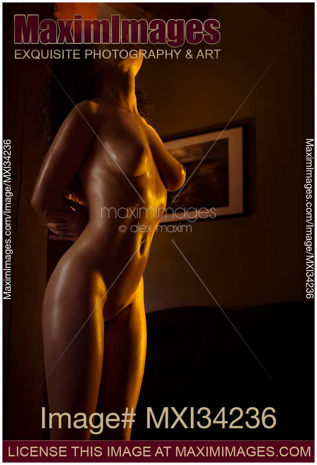 Beautiful nude woman with shiny golden skin leaning against a wooden pillar in a dark room