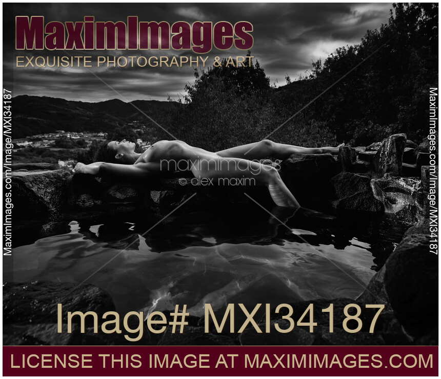 Beautiful nude woman with wet sexy naked body lying on rocks on the edge of onsen hot spring pool. Black and white photograph.