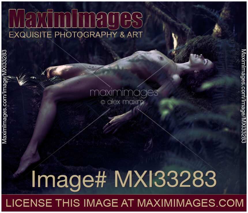Beautiful nude woman with wet shiny body lying naked on a mossy tree trunk in dark dramatic forest nature scenery