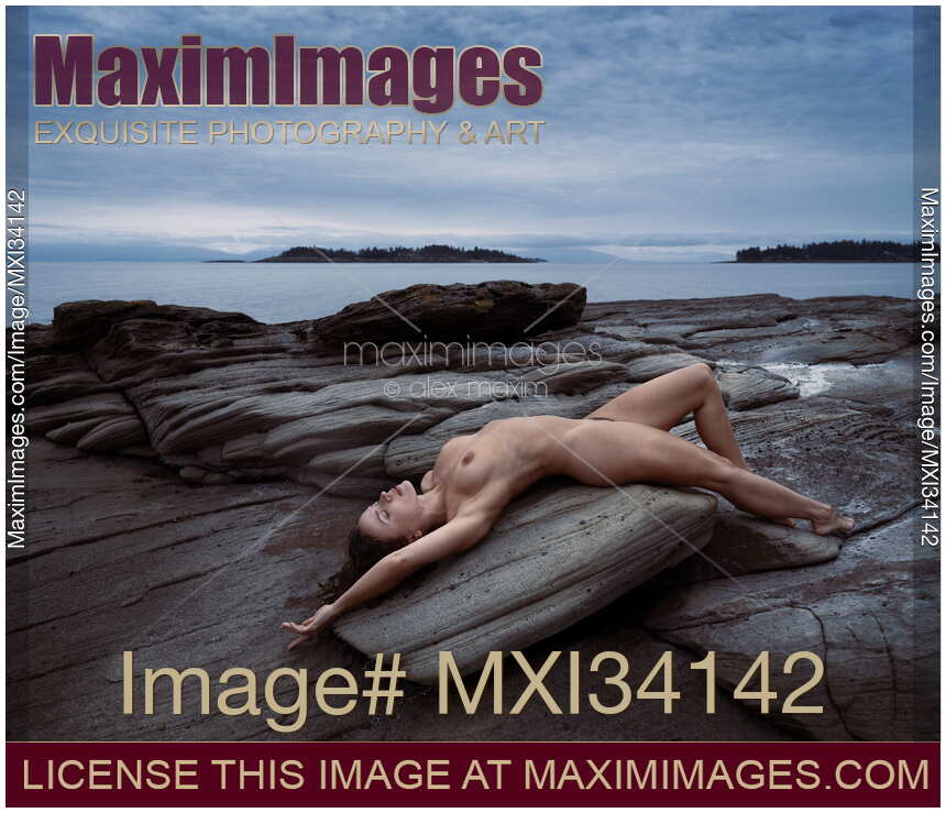 Beautiful nude young woman lying naked stretched on ocean shore rock in graceful relaxed pose in nature scenery