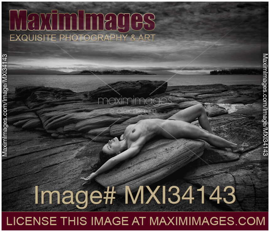 Beautiful nude young woman lying naked stretched on ocean shore rock in graceful relaxed pose Black and white