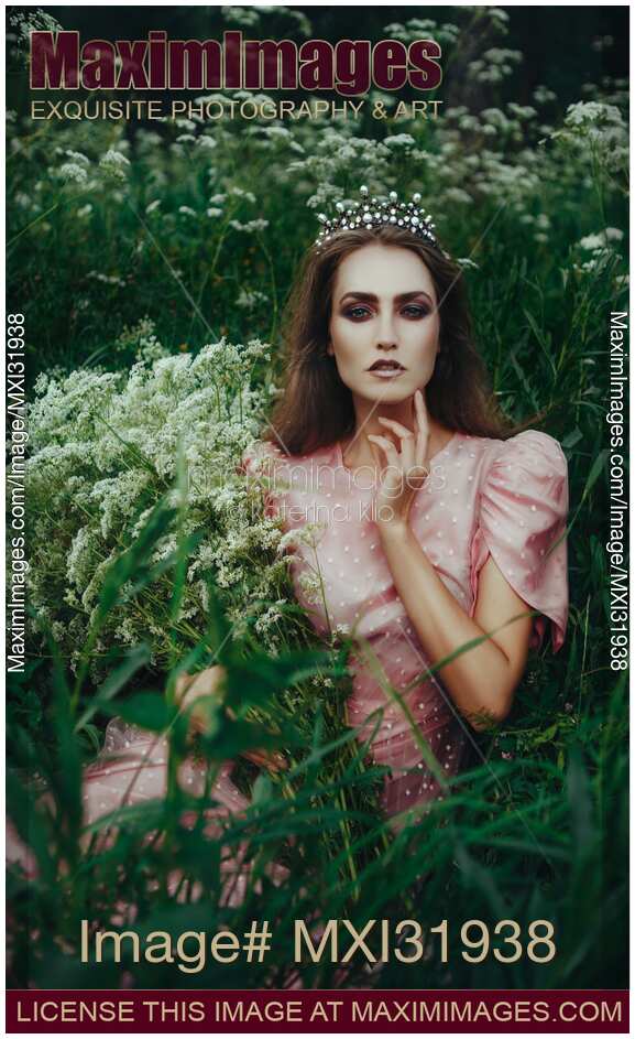 Beautiful princess in a crown sitting in a field of wild yarrow with flowers in her hands
