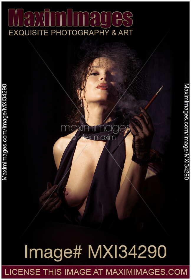 Beautiful seductive femme fatale lady in black dress and veil exposing her breast and exhaling cigarette smoke